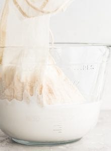 A glass jar of homemade almond milk with a nut milk bag in it.