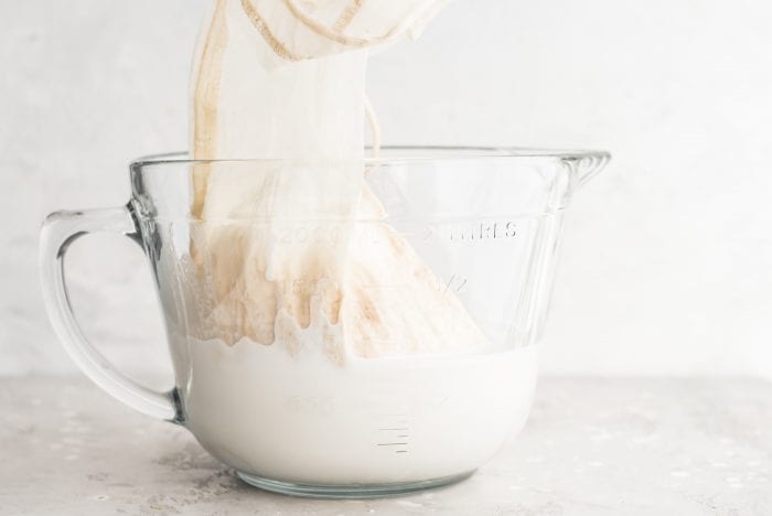 Blended almond milk and a nut milk bag in a large glass measuring cup.