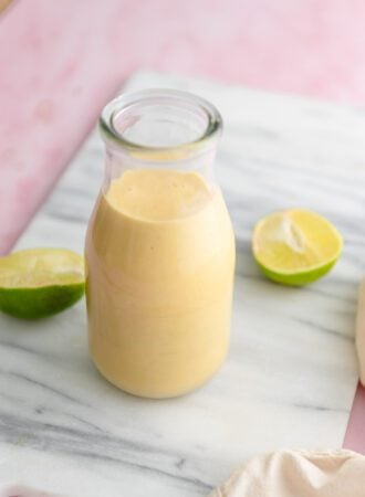 Creamy mango coconut smoothie in a glass milk jar on a marble cutting board with two lime halves beside the glass.
