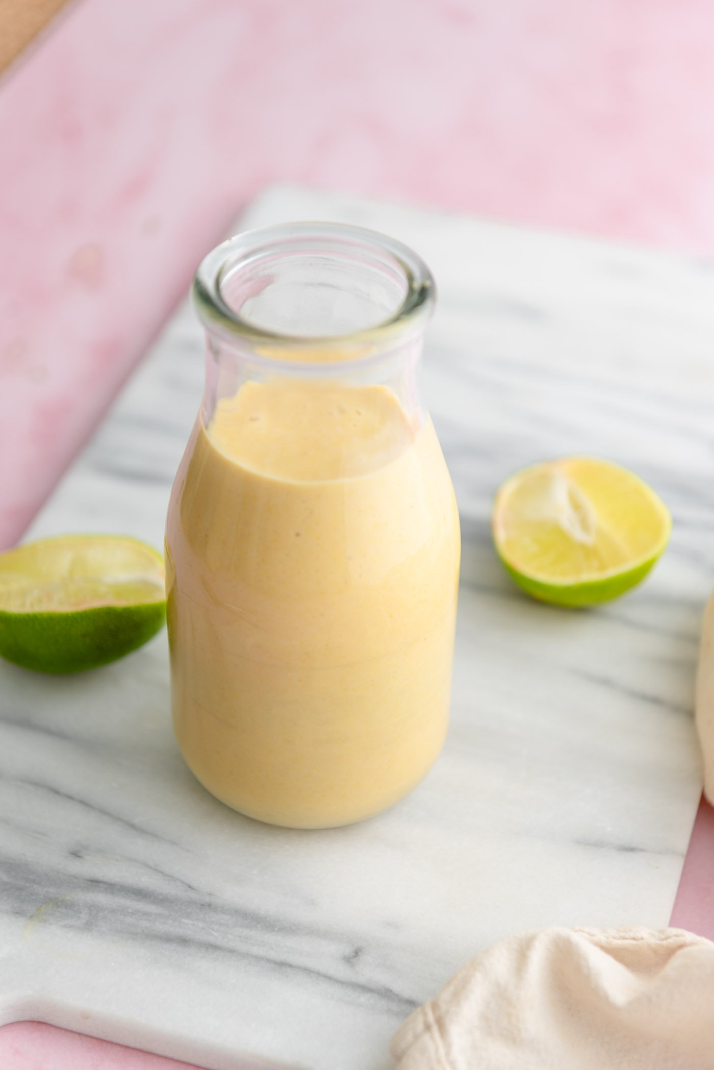 Creamy mango coconut smoothie in a glass milk jar on a marble cutting board with two lime halves beside the glass.