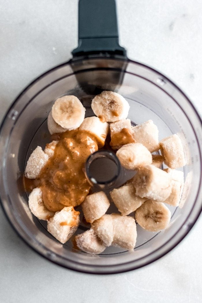 Food processor with frozen chopped banana and peanut butter in it.