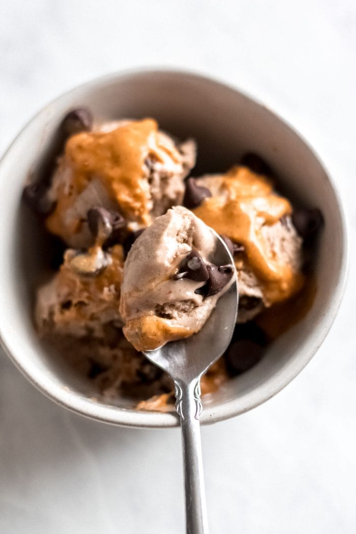 A small spoon scooping chocolate ice cream form a bowl of ice cream topped with chocolate chips and caramel sauce.