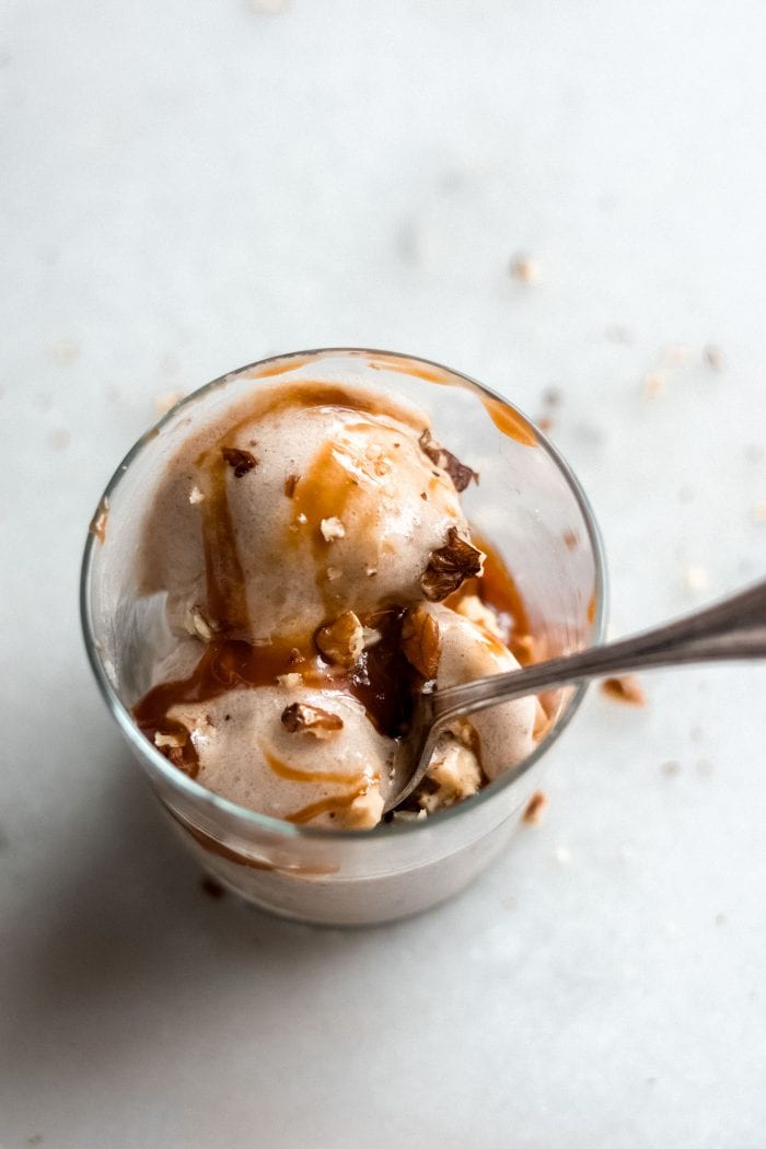 Glass filled with vegan banana ice cream topped with nuts and caramel sauce.