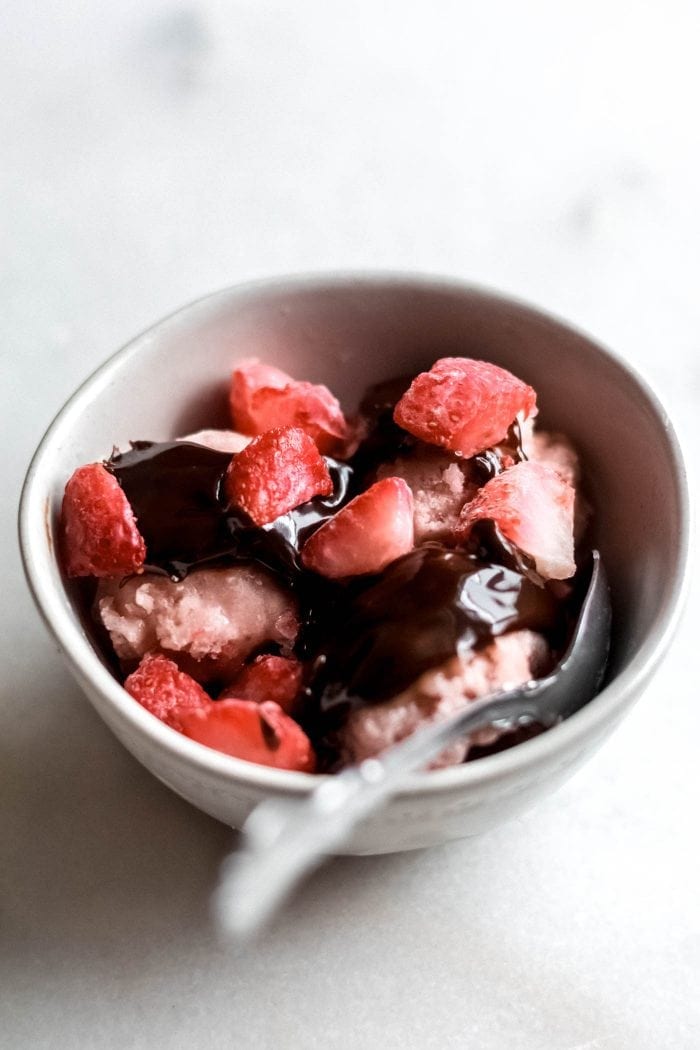 A small bowl of strawberry ice cream with chocolate sauce and chopped strawberries on top.