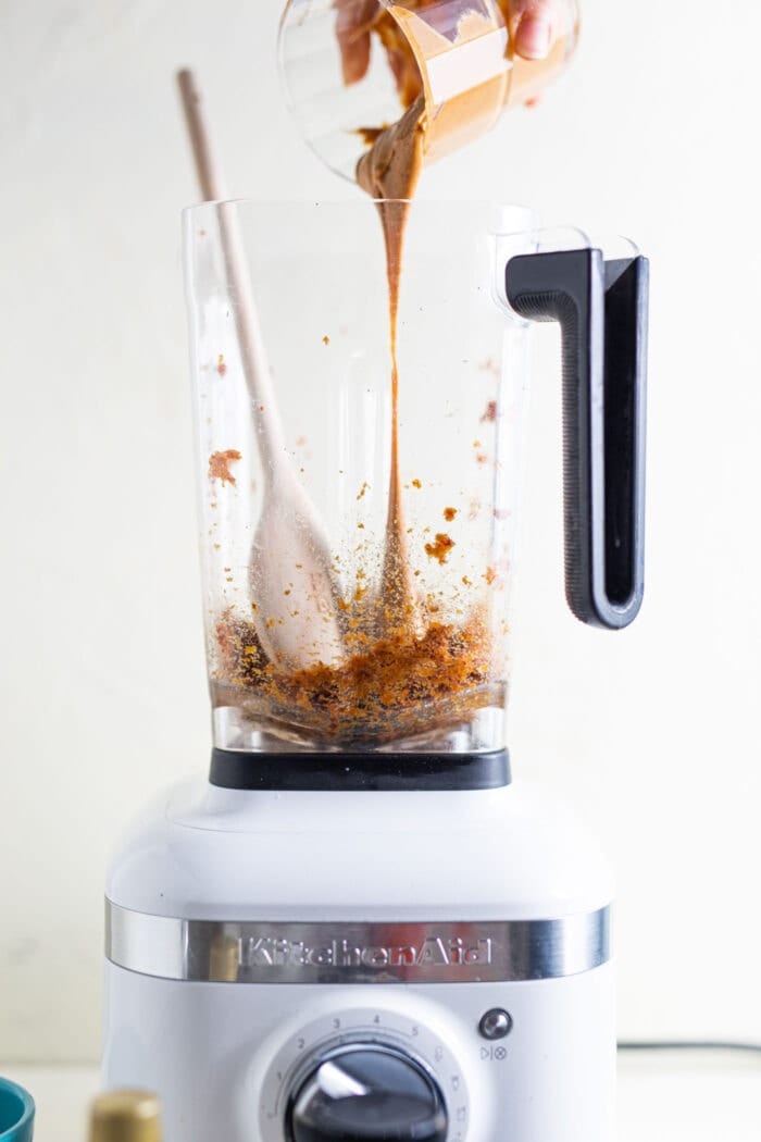Almond butter being poured into a blender with blended dates in it.
