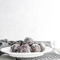 A plate of chocolate balls rolled in shredded coconut sitting on a baking cooling rack.