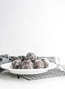 A plate of chocolate balls rolled in shredded coconut sitting on a baking cooling rack.