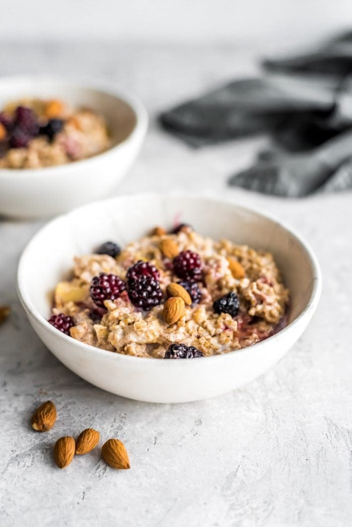 Hot oven baked steel cut oats in two small bowls with blackberries and almonds.