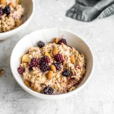 Oven baked steel cut oats in a small bowl with blackberries, maple syrup, almond milk and almonds.