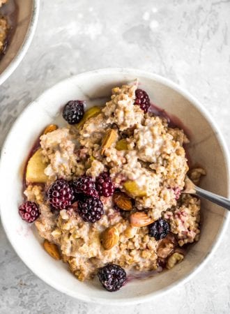 Oven baked steel cut oats in a small bowl with blackberries, maple syrup, almond milk and almonds.
