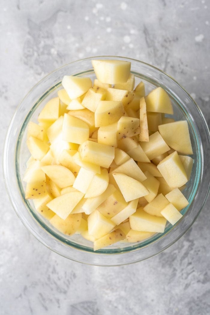 Raw cubed potatoes in a glass mixing bowl.