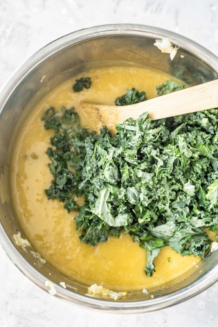 Overhead shot of creamy potato soup in an Instant Pot with raw kale being mixed.
