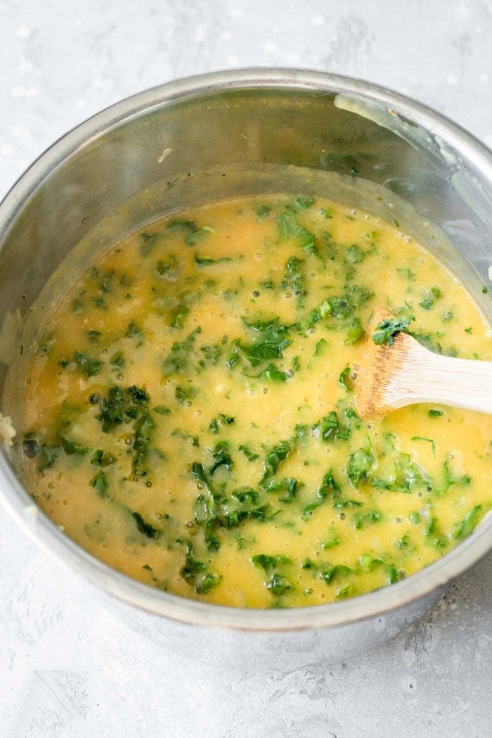 Creamy kale potato soup in an Instant Pot with a wooded spoon.