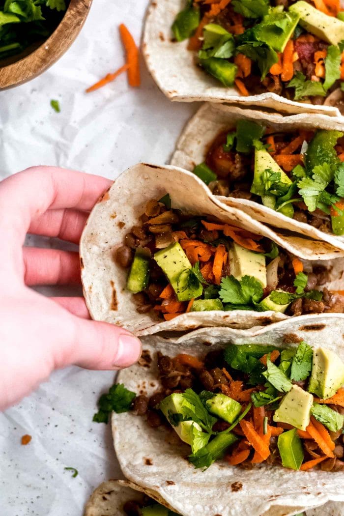 Hand picking up a vegan lentil taco with avocado, carrot and salsa.