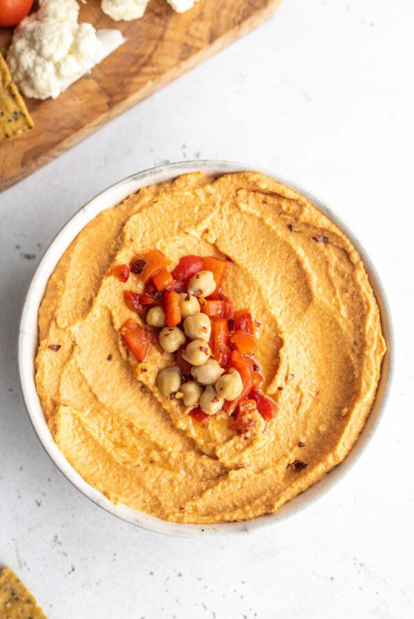 Overhead close up shot of roasted red pepper hummus topped with chickpeas, roasted red peppers and red pepper flakes.