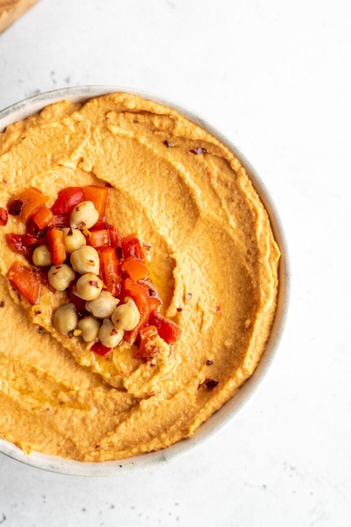 Overhead close up shot of roasted red pepper hummus topped with chickpeas, roasted red peppers and red pepper flakes.