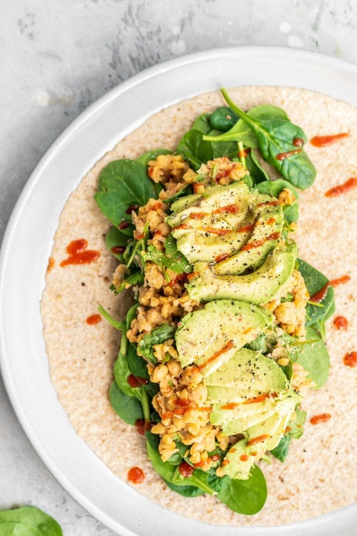Chickpea salad, avocado and spinach in a tortilla topped with a drizzle of hot sauce to make a spicy chickpea wrap.
