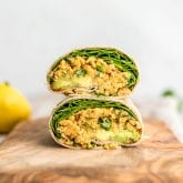 Two stacked halves of a chickpea salad, avocado and spinach wrap cut on a cutting board.