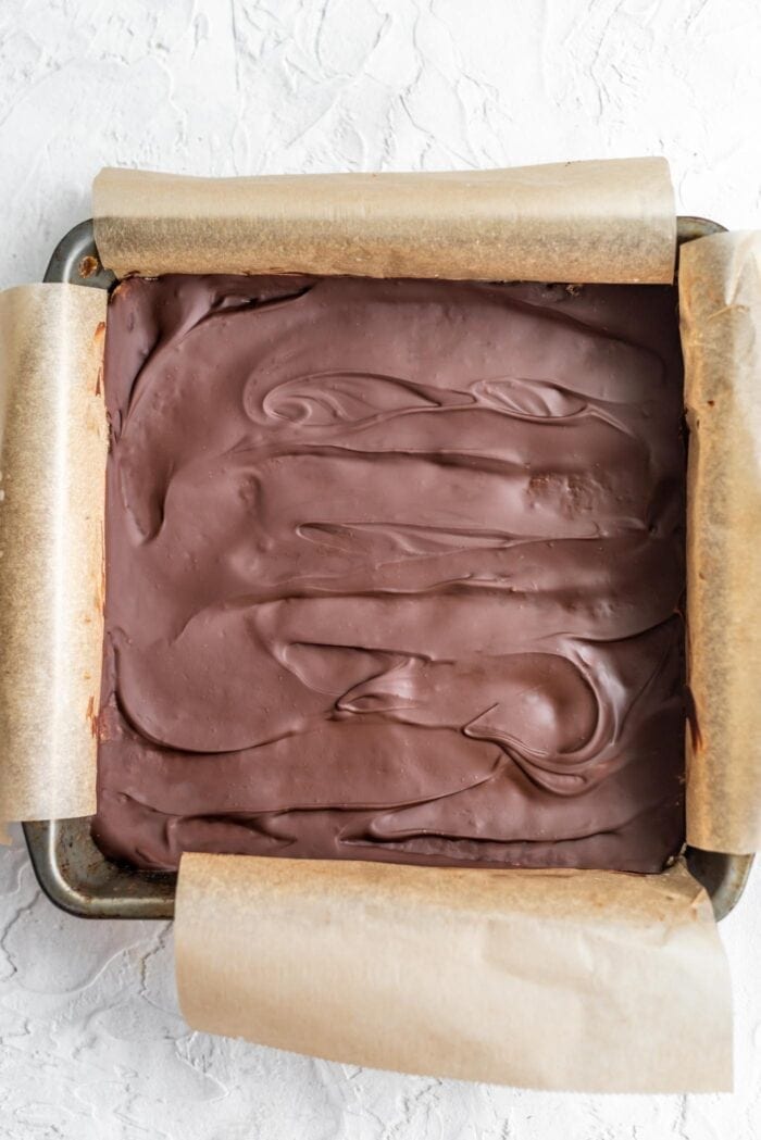 Chocolate-covered coconut bars in a baking pan lined with parchment paper.
