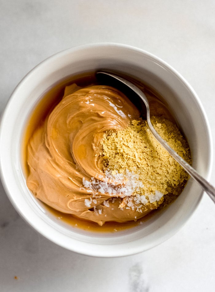 Peanut butter, nutritional yeast and coconut oil in a bowl with a spoon.