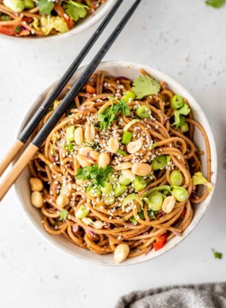 A bowl of noodles topped with green onions, peanuts and cilantro with a set of chopsticks sitting on the bowl.