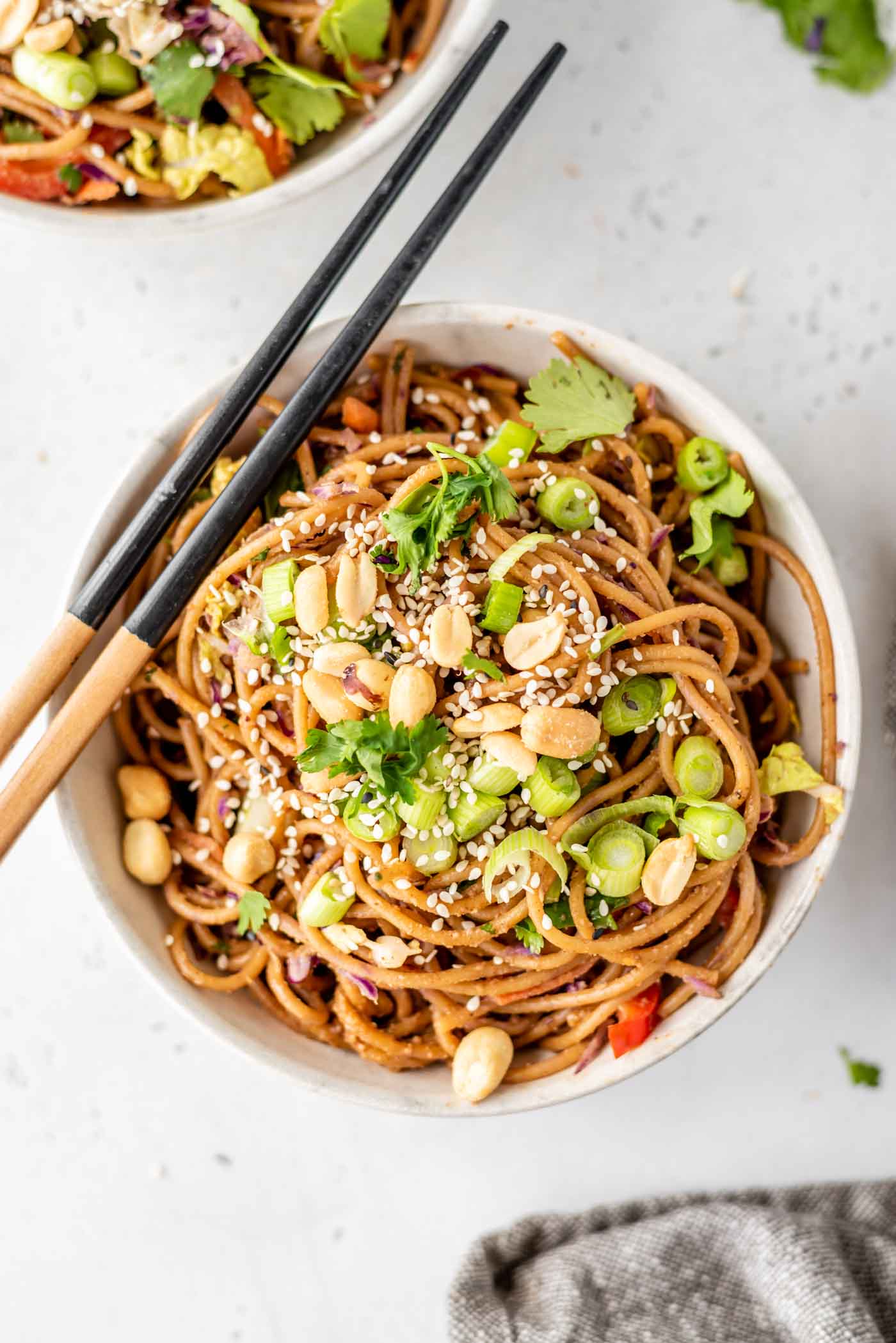 A bowl of noodles topped with green onions, peanuts and cilantro with a set of chopsticks sitting on the bowl.
