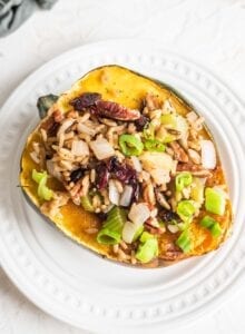 A brown rice, celery and cranberry stuffed acorn squash on a small white plate.