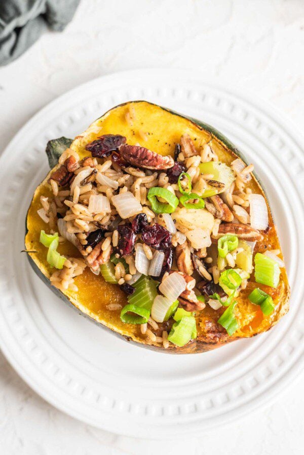 A brown rice, celery and cranberry stuffed acorn squash on a small white plate.