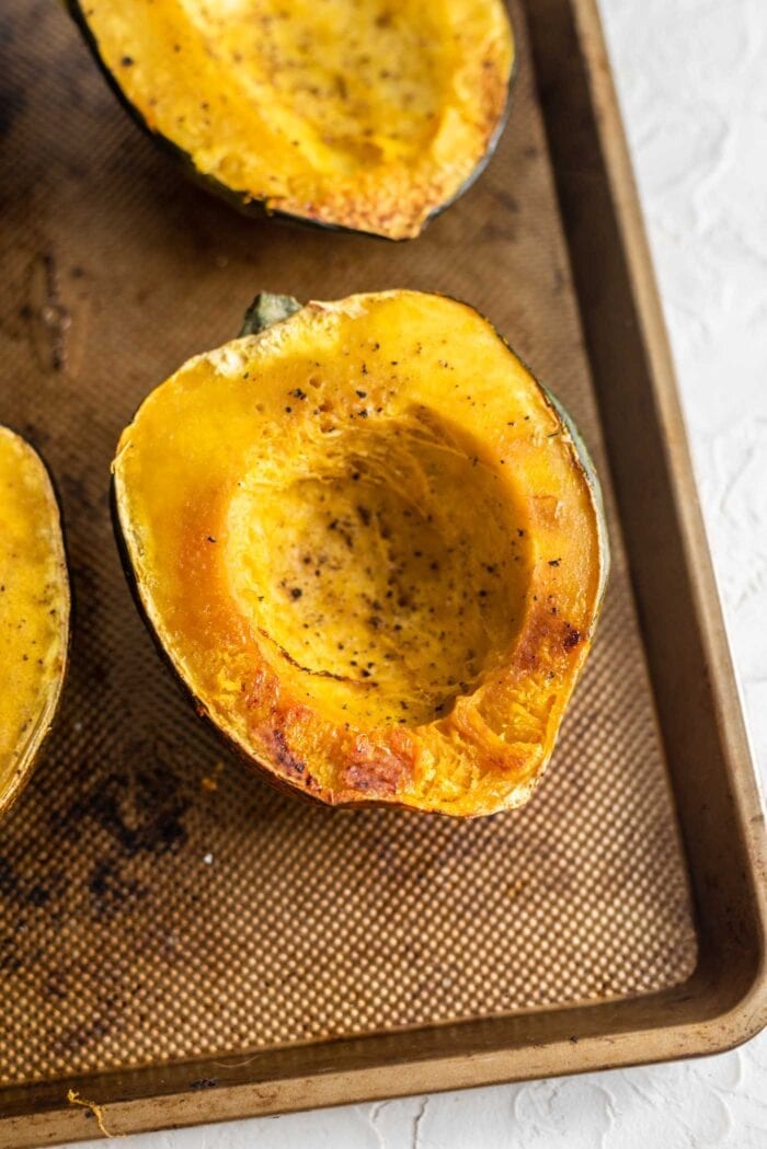 Half of a roasted acorn squash sprinkled with salt and pepper on a baking tray.