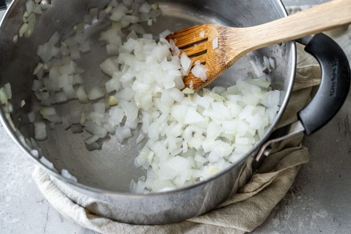 Diced onion and garlic in a soup pot being stirred with a wooden spoon.