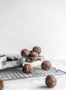 Vegan no-bake chocolate cashew coconut balls in a glass dish sitting on a cooling rack.