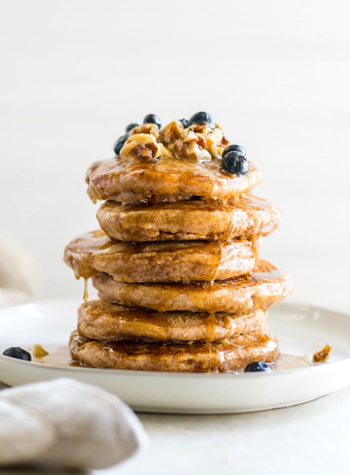 A stack of vegan pancakes topped with berries and maple syrup.