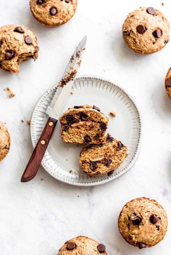 Sliced chocolate chip banana muffin filled with almond butter on a small, white plate with a knife.