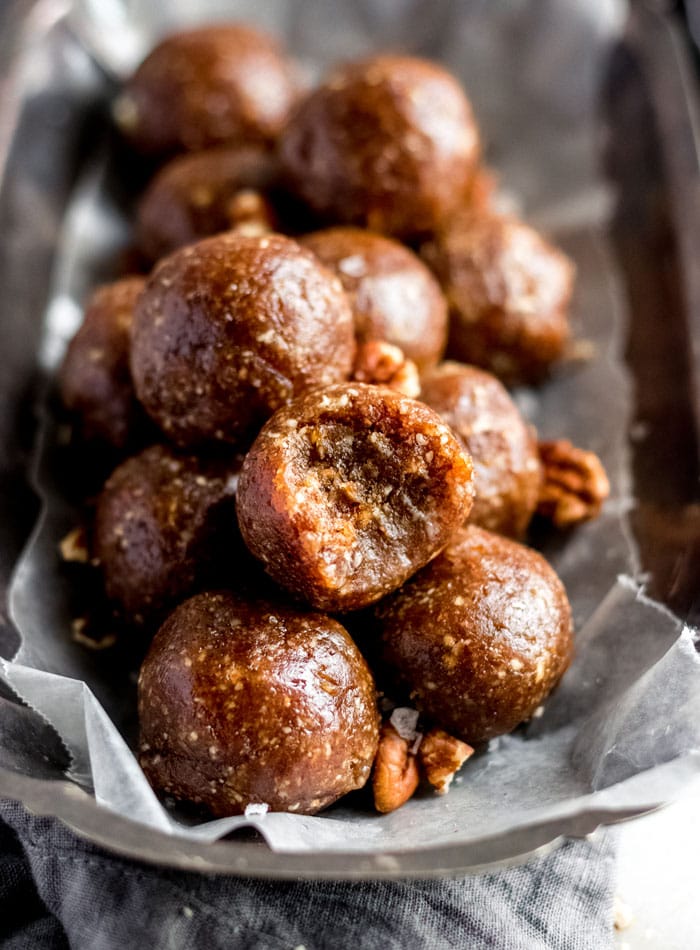 A number of no-bake pecan balls on a small tray lined with parchment paper. The ball on top has a bite taken from it.