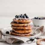 Stack of vegan blueberry coconut pancake with blueberries and coconut on top.