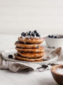 Stack of vegan blueberry coconut pancake with blueberries and coconut on top.