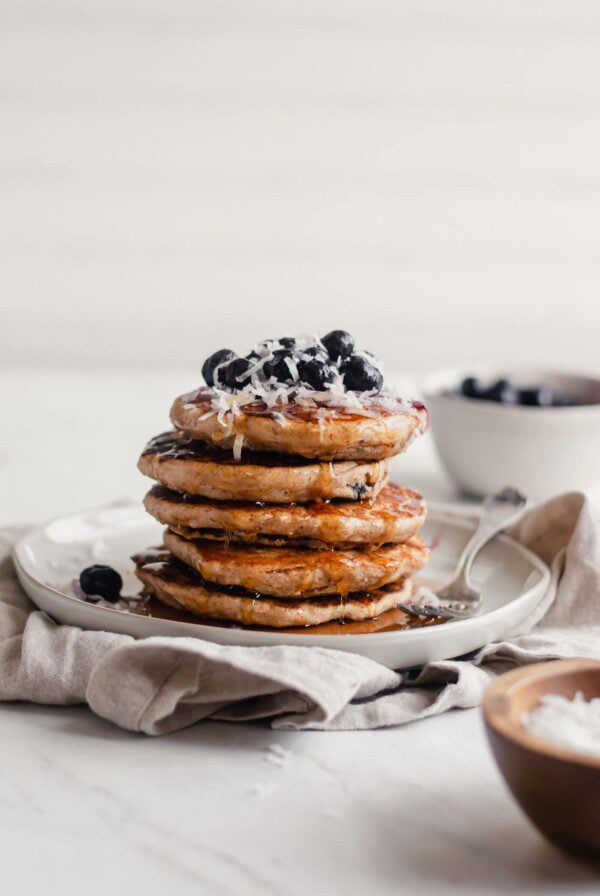 Stack of vegan blueberry coconut pancake with blueberries and coconut on top.