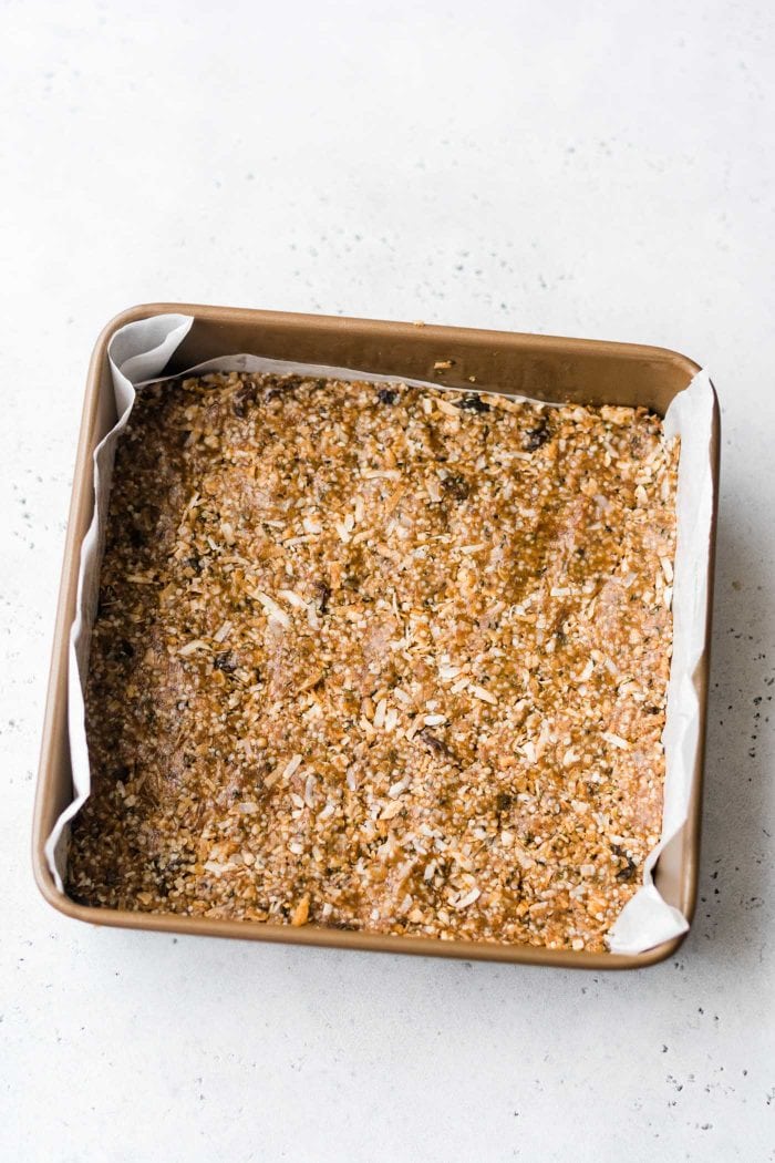 Paleo energy bars with coconut and hemp seeds in a metal baking pan lined with parchment paper.