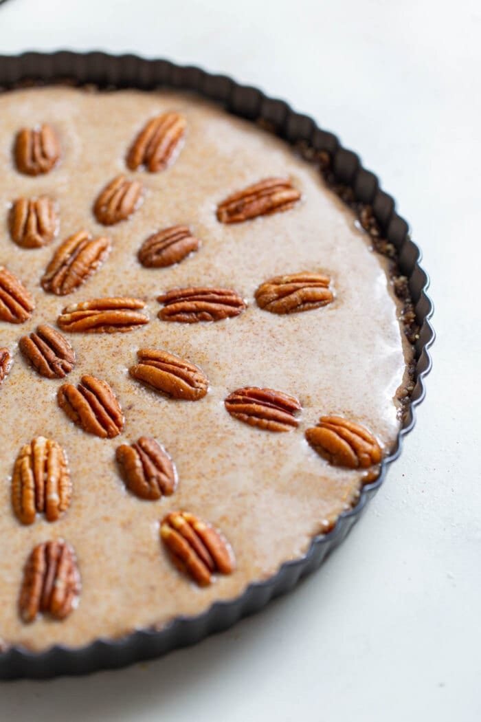Raw vegan maple pecan pie in a pie dish topped with pecans.