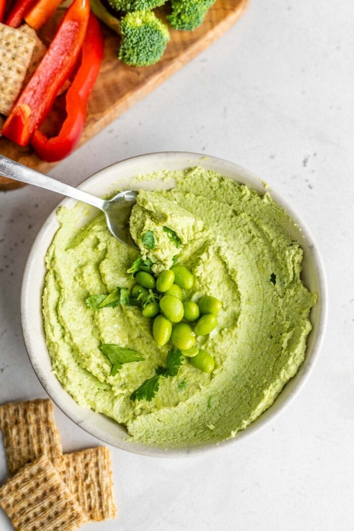 A bowl of edamame hummus topped with edamame beans and cilantro.
