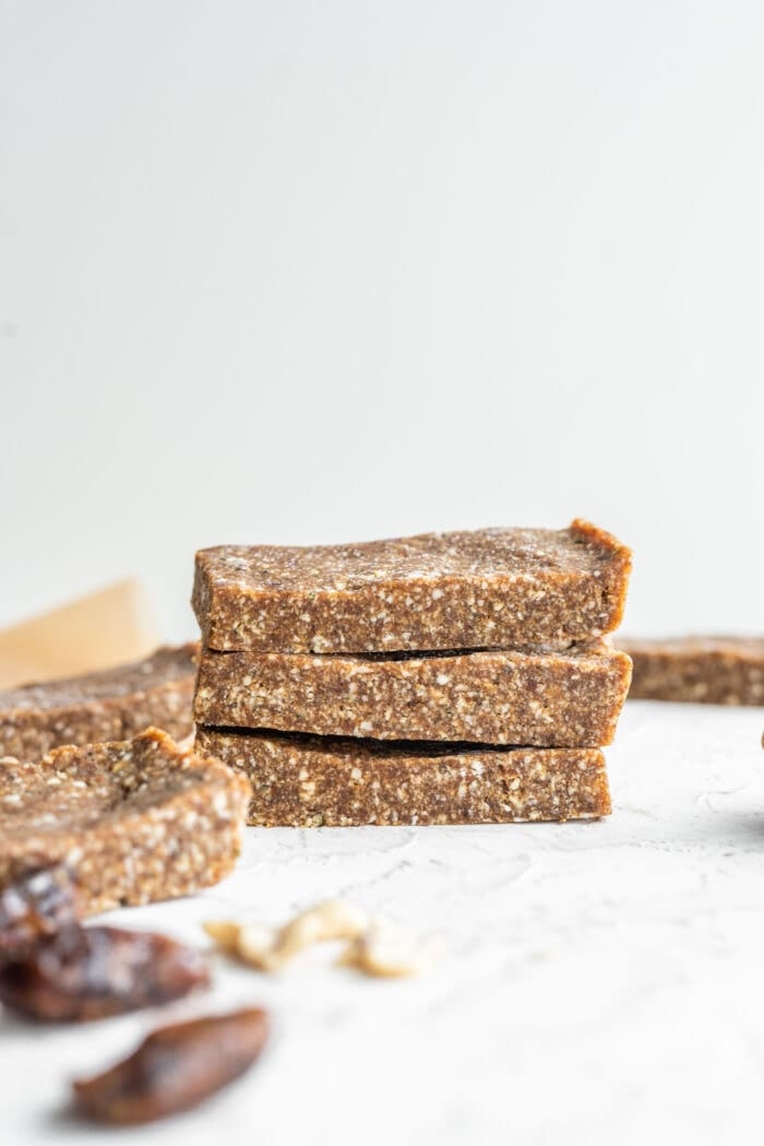 Stack of 3 paleo energy bars with a few more bars and dates scattered and out of focus in the background and foreground.