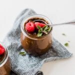 Small glass jar of vegan chocolate avocado pudding topped with raspberries and mint.