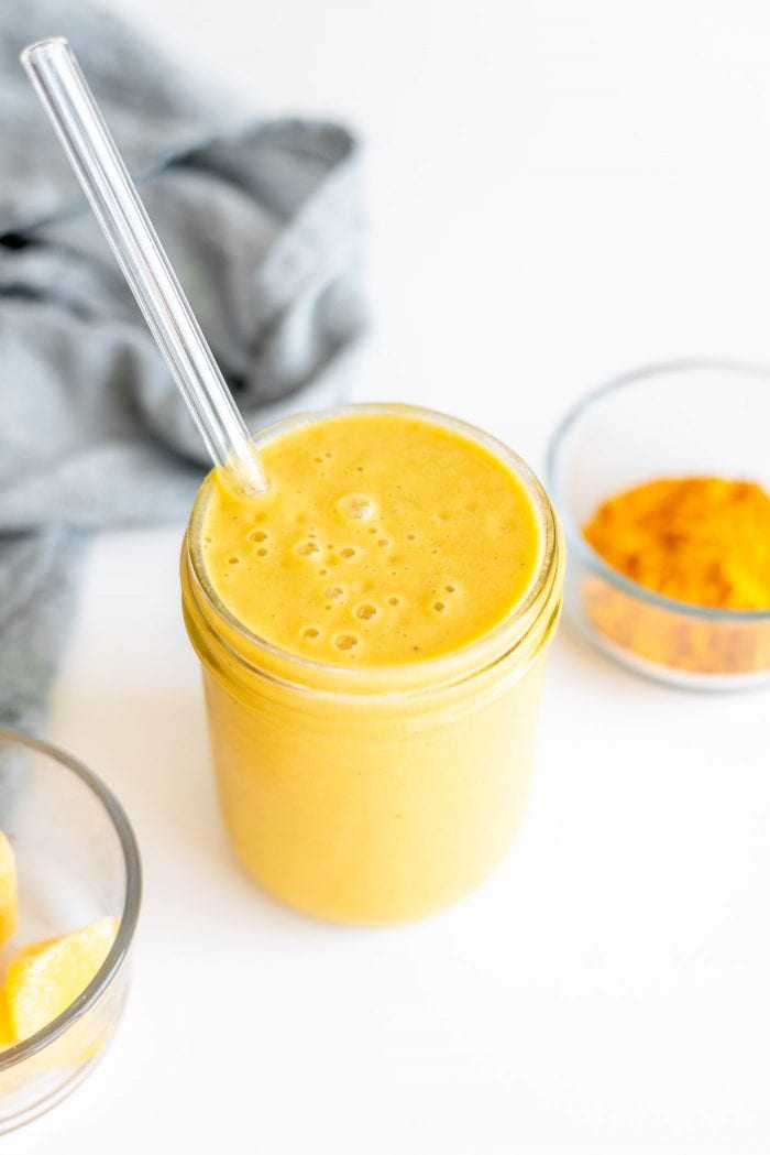 A vegan orange mango smoothie in a glass mason jar with a straw.