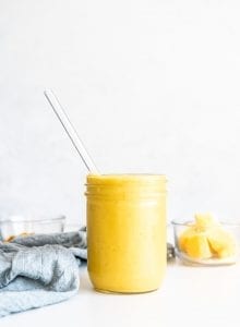 An orange mango smoothie in a mason jar with a glass straw.