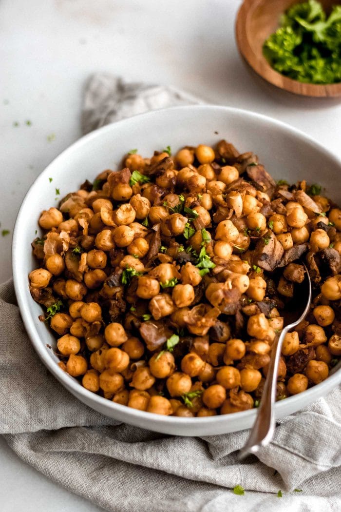 Easy vegan spiced chickpeas with mushroom and garlic in a white bowl with a spoon.