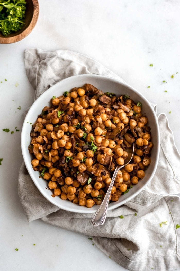 Vegan spiced chickpeas with mushroom and onion in a white bowl with a serving spoon.
