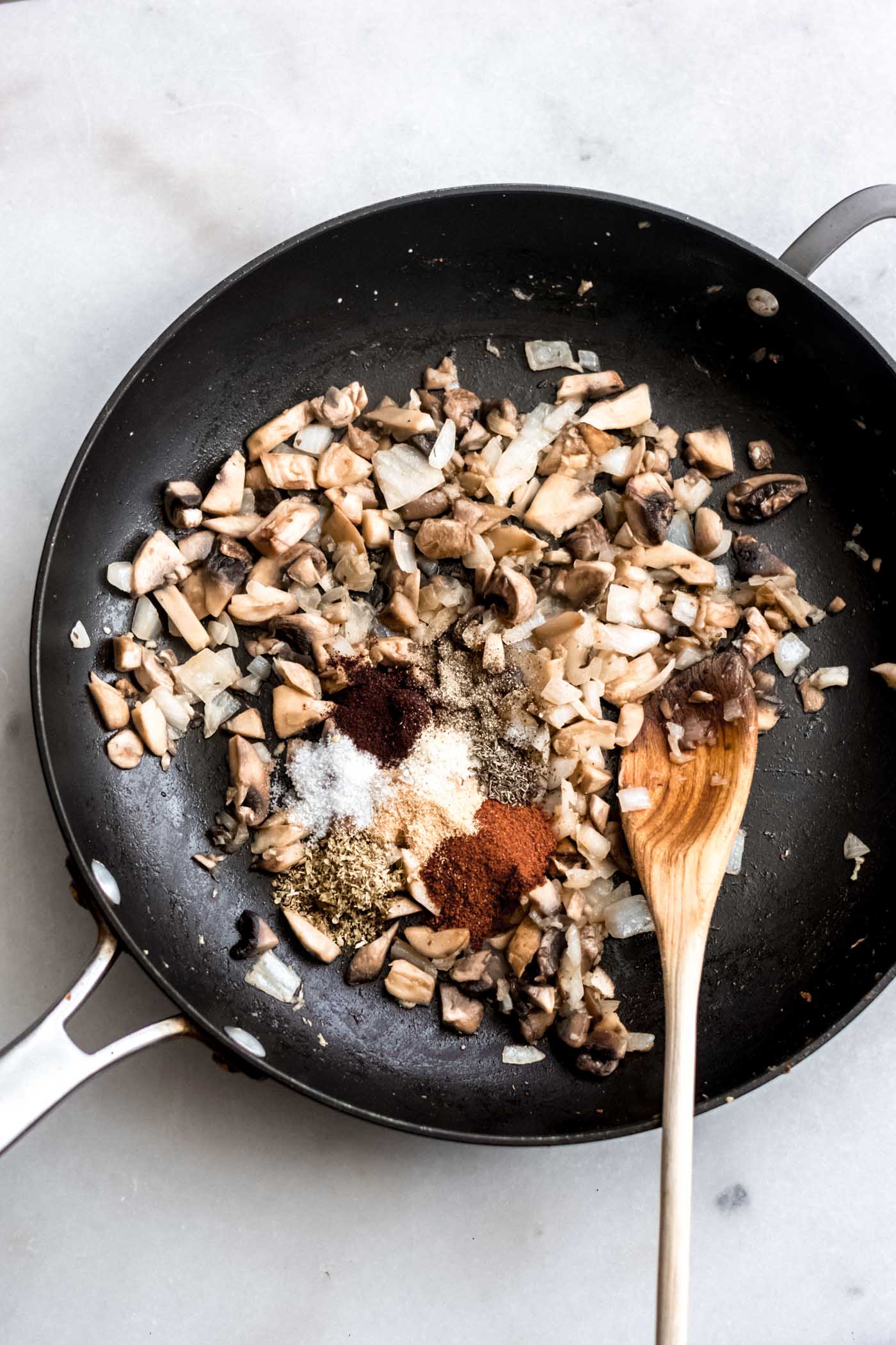 Mushrooms, onions and spices in a skillet with a wooden spoon for making spiced chickpeas.