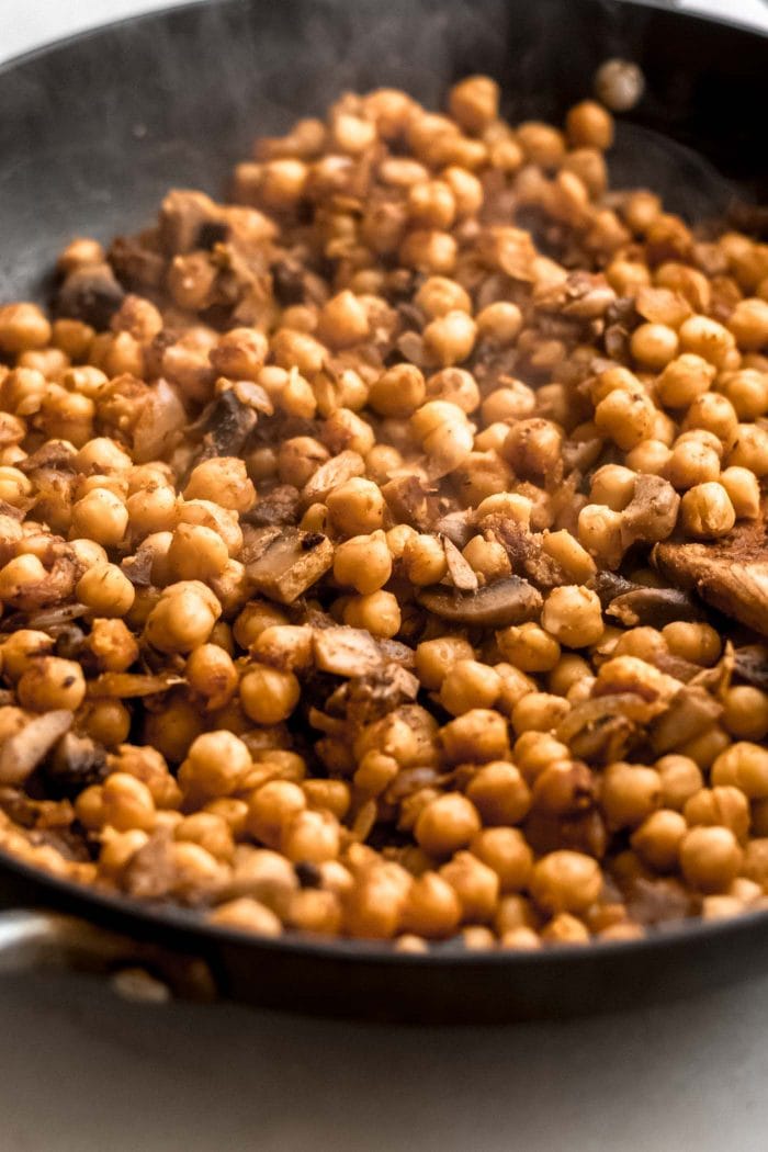 Spiced chickpeas in a skillet with a wooden spoon.
