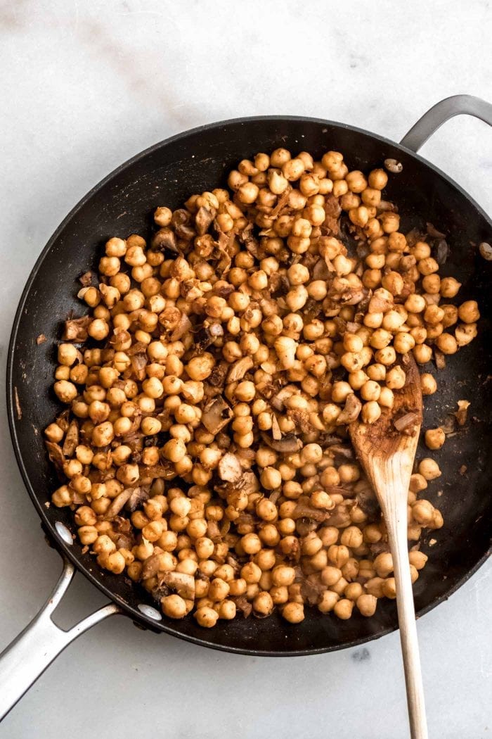 Seasoned chickpeas in a pan with a wooden spoon.