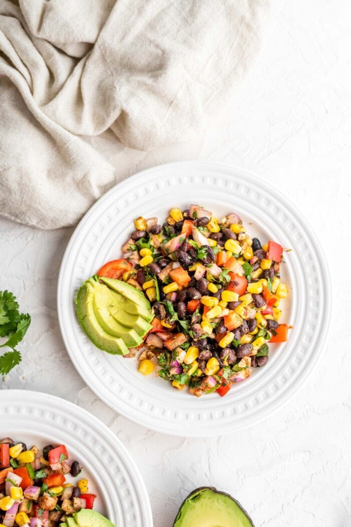 A small plate of black bean corn salad with bell pepper and red onion with a few slices of avocado on the plate.